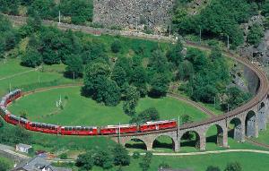 Small red train climbs a circle viaduct.