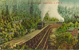 Steam passenger train on huge wooden trestle, doubleheaded and with pusher.